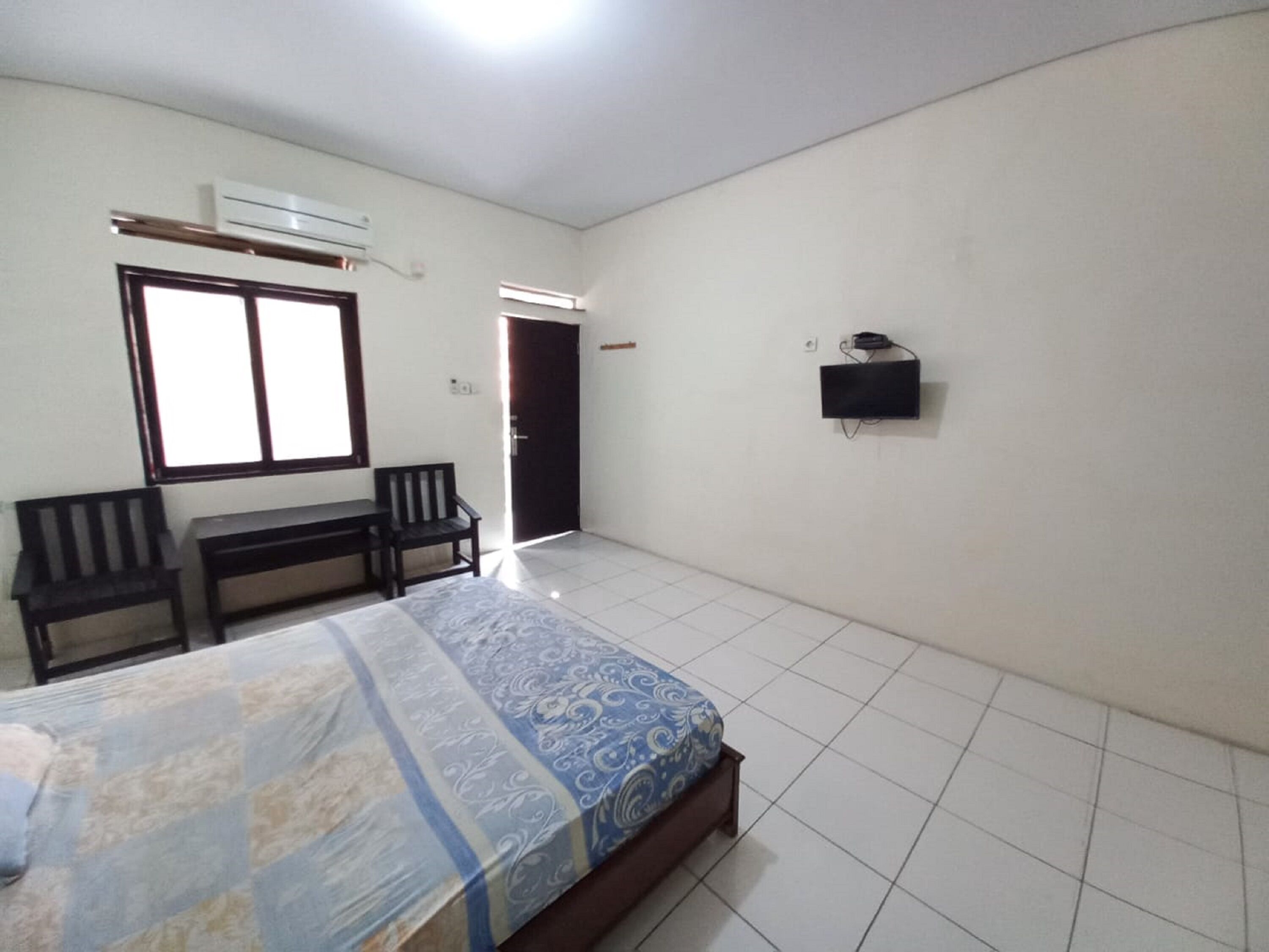 A bedroom with a bed, a desk, two chairs, a TV, and a door.