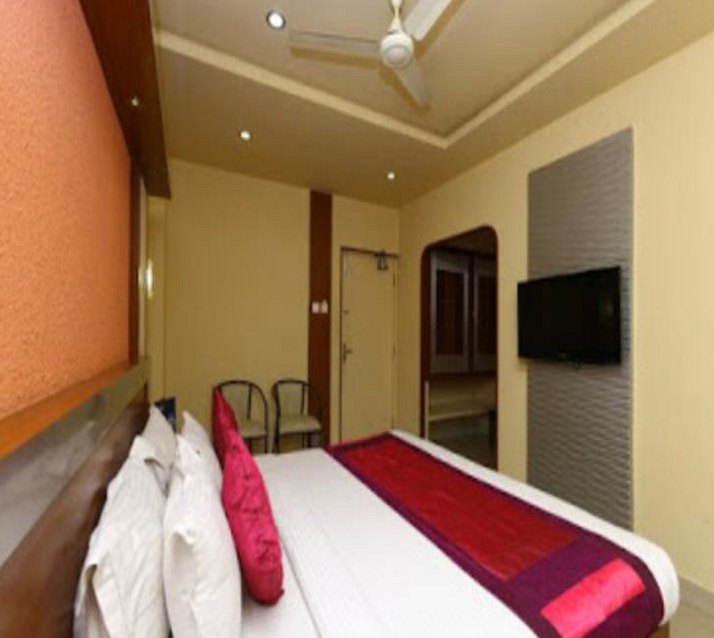 A hotel room with a bed, a ceiling fan, a television on the wall, and a door leading to another room.