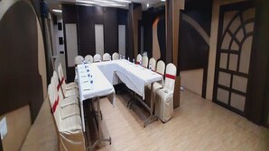 A conference room with a long table, chairs, and a stage area. - Navaratna Delight (Coimbatore)