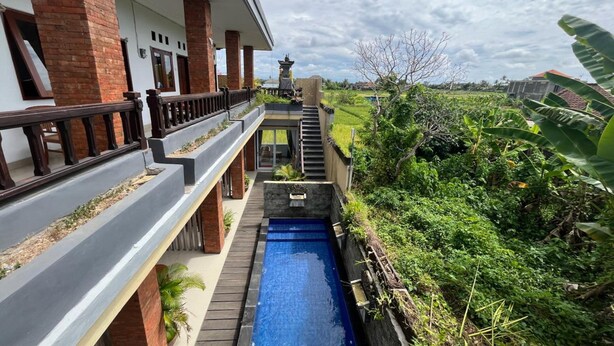 Propiedad residencial con piscina, una escalera que lleva al segundo piso y vista a un paisaje verde exuberante.