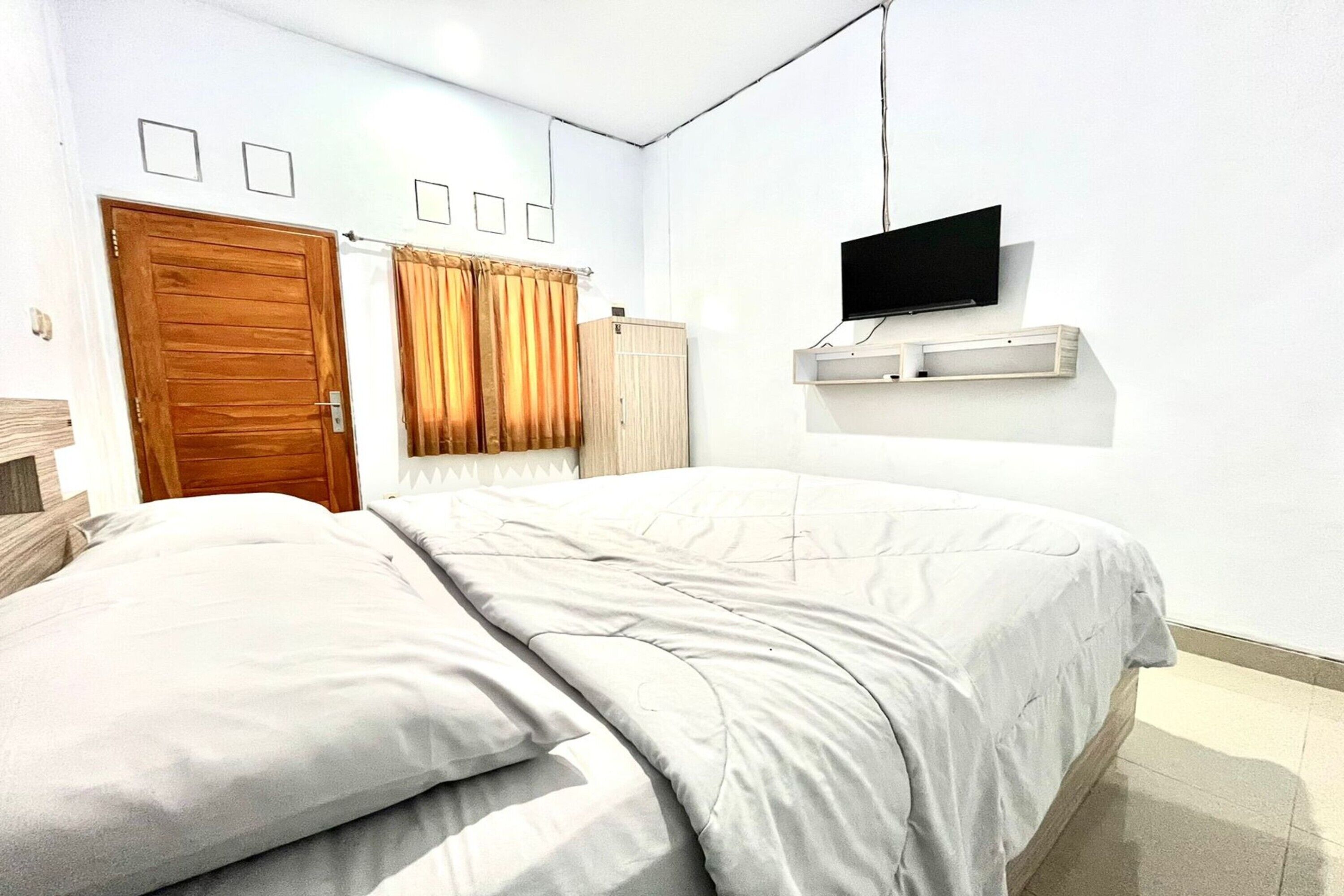 A bedroom with a bed, a television mounted on the wall, and a wooden wardrobe.