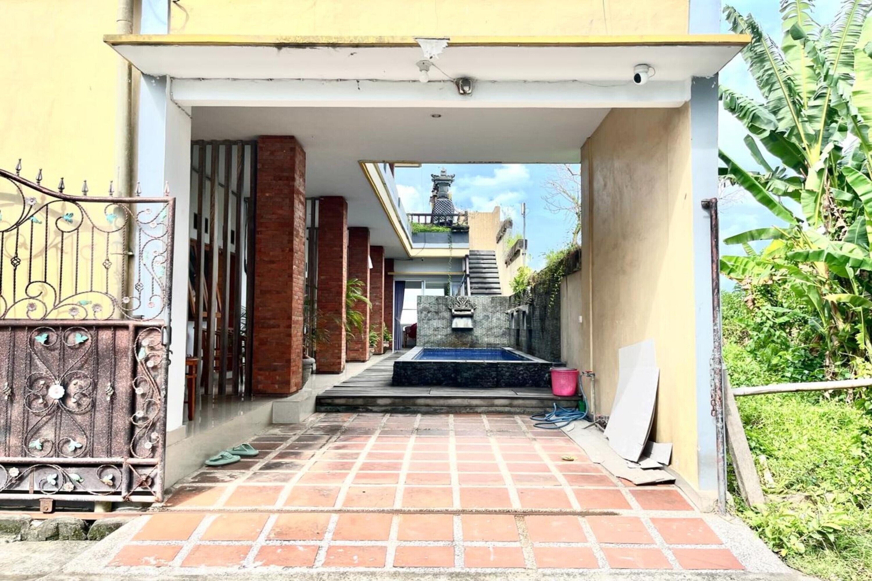 Un camino que lleva a un edificio con entrada de azulejos, una puerta de metal y una pequeña zona de piscina.