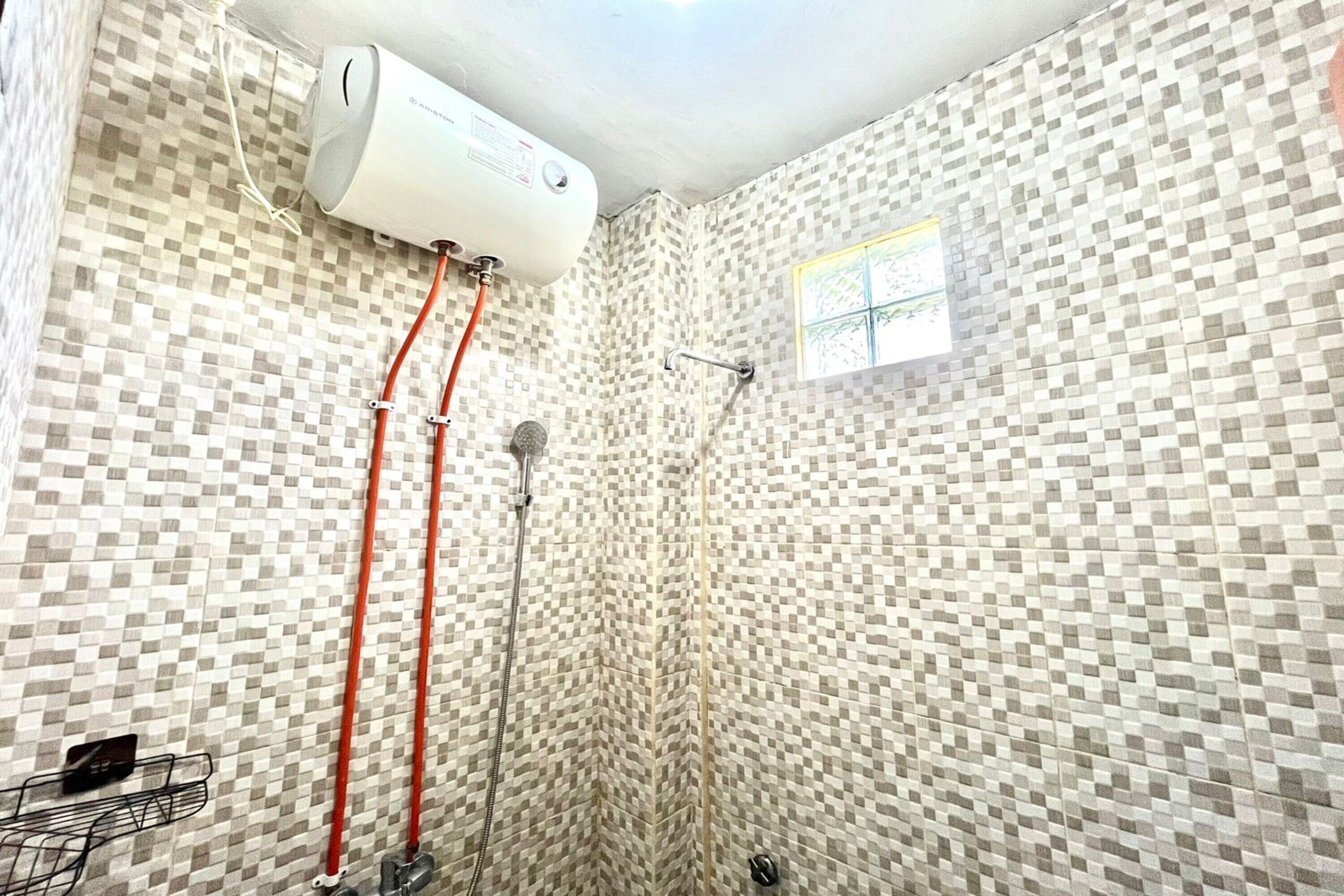 A shower with a checkered tile wall, a window, and a water heater mounted on the wall.