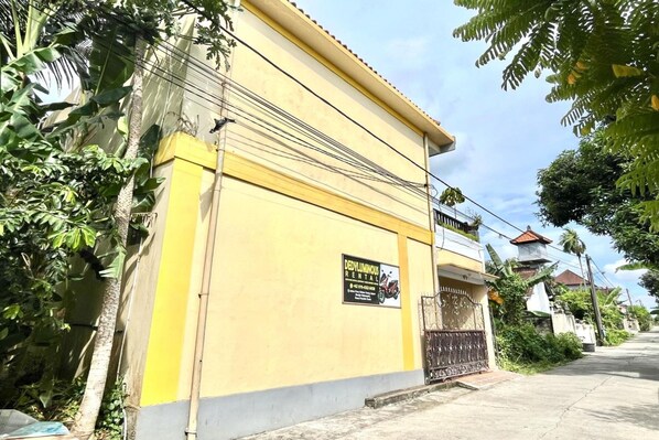 A yellow building with a rental sign, surrounded by greenery and a clear sky.