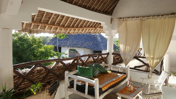 A balcony with a thatched roof, white furniture, and a view of lush greenery. - Safina Beach House (Watamu)