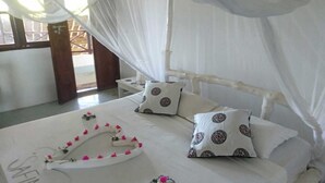 A bed with white bedding, two pillows with circular patterns, and a decorative floral arrangement on the bed. - Safina Beach House (Watamu)