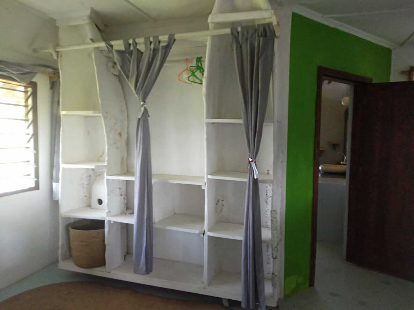 A room with a white shelving unit, grey curtains, a green wall, and a wooden door.
