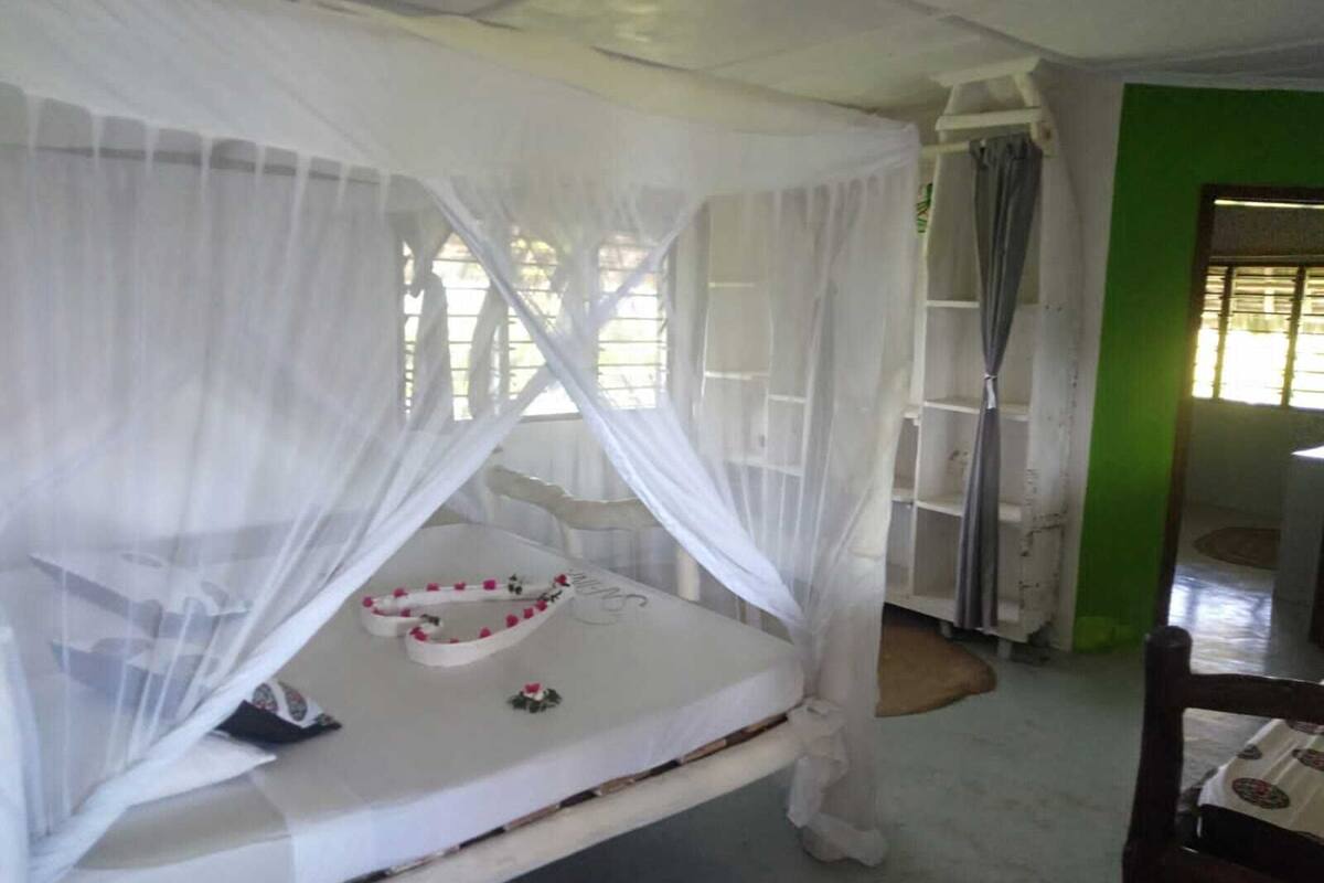 Ein Zimmer mit einem Bett unter einem weißen Baldachin, einem kleinen Tisch mit einer Dekoration und einer grünen Wand.