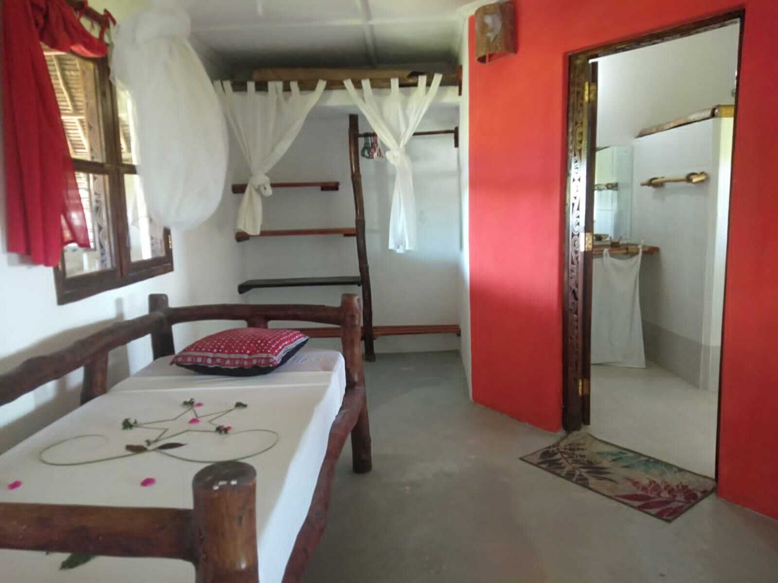 A room with a bed, a wooden chair, a window with red curtains, a white canopy, a ladder, and a bathroom with a mirror and towel rack.