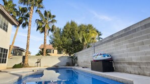 Una piscina con un muro de hormigón, palmeras y un edificio pequeño al fondo.