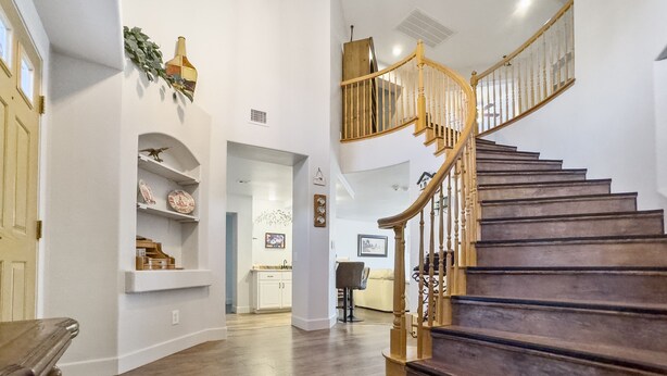 Un interior amplio con una escalera de madera, paredes blancas y una cocina visible al fondo.