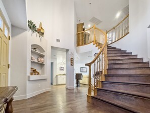 A spacious interior with a wooden staircase, white walls, and a kitchen area visible in the background.