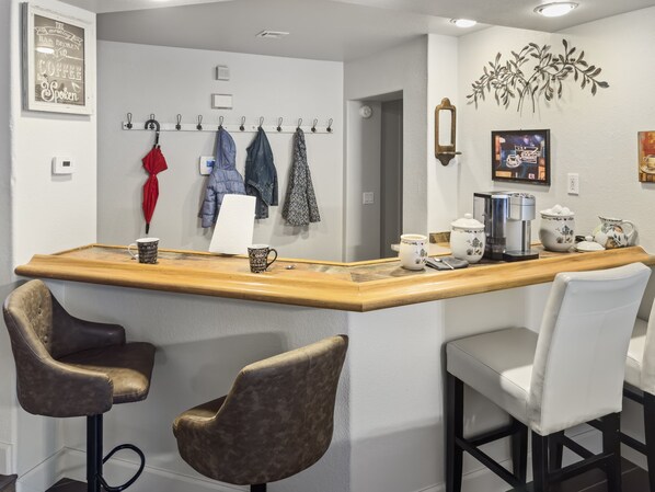 A kitchen with a bar area, featuring a coffee machine, mugs, and a variety of kitchen utensils.