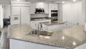Una cocina moderna con armarios blancos, encimeras de granito, electrodomésticos de acero inoxidable y una isla central con lavamanos.