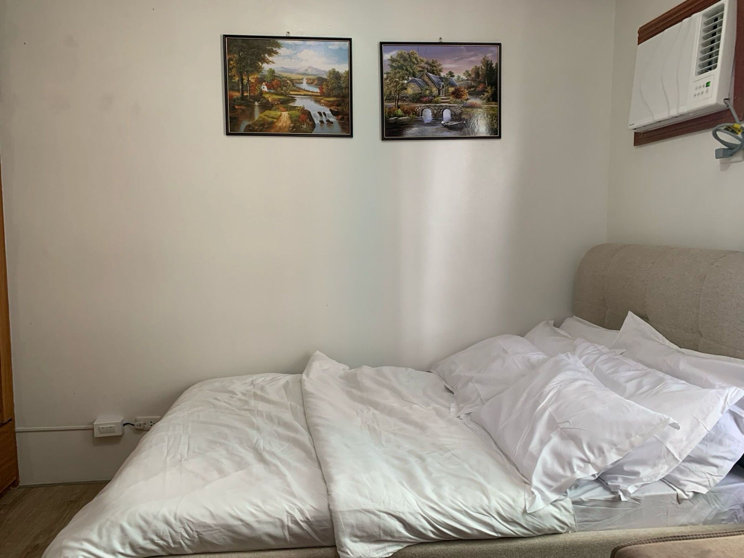 A bedroom with a bed, white bedding, and two landscape paintings on the wall.