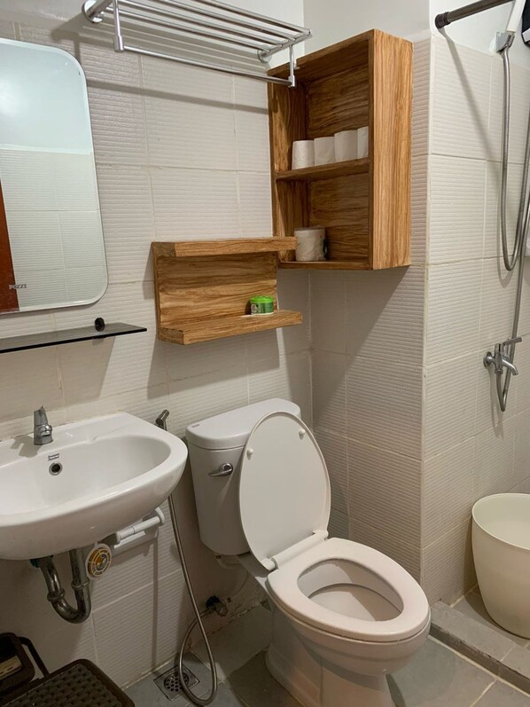 A bathroom with a toilet, sink, and shower. There are wooden shelves above the toilet and a towel rack above the sink. - Urban Haven in Bacolod City (Bacolod)