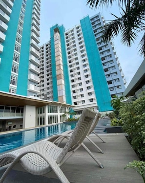 A poolside area with lounge chairs, a swimming pool, and high-rise buildings in the background. - Urban Haven in Bacolod City (Bacolod)