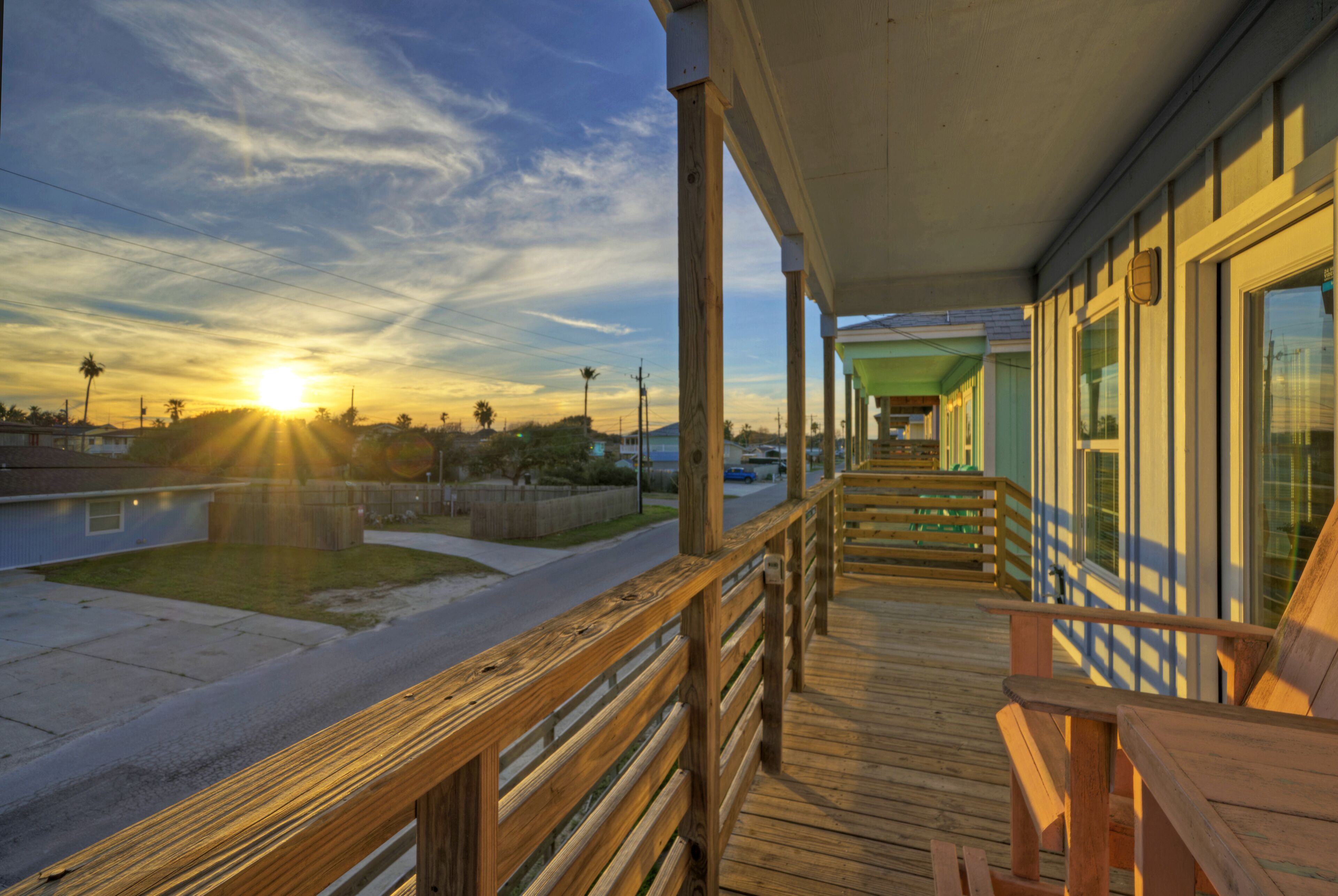 Una terraza de madera con baranda, un banco y vistas a la puesta de sol sobre el agua.