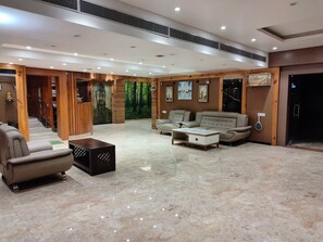 A spacious lobby with a marble floor, a staircase, a Buddha statue, and a seating area with sofas and a coffee table. - Rupam Tower (Patna)