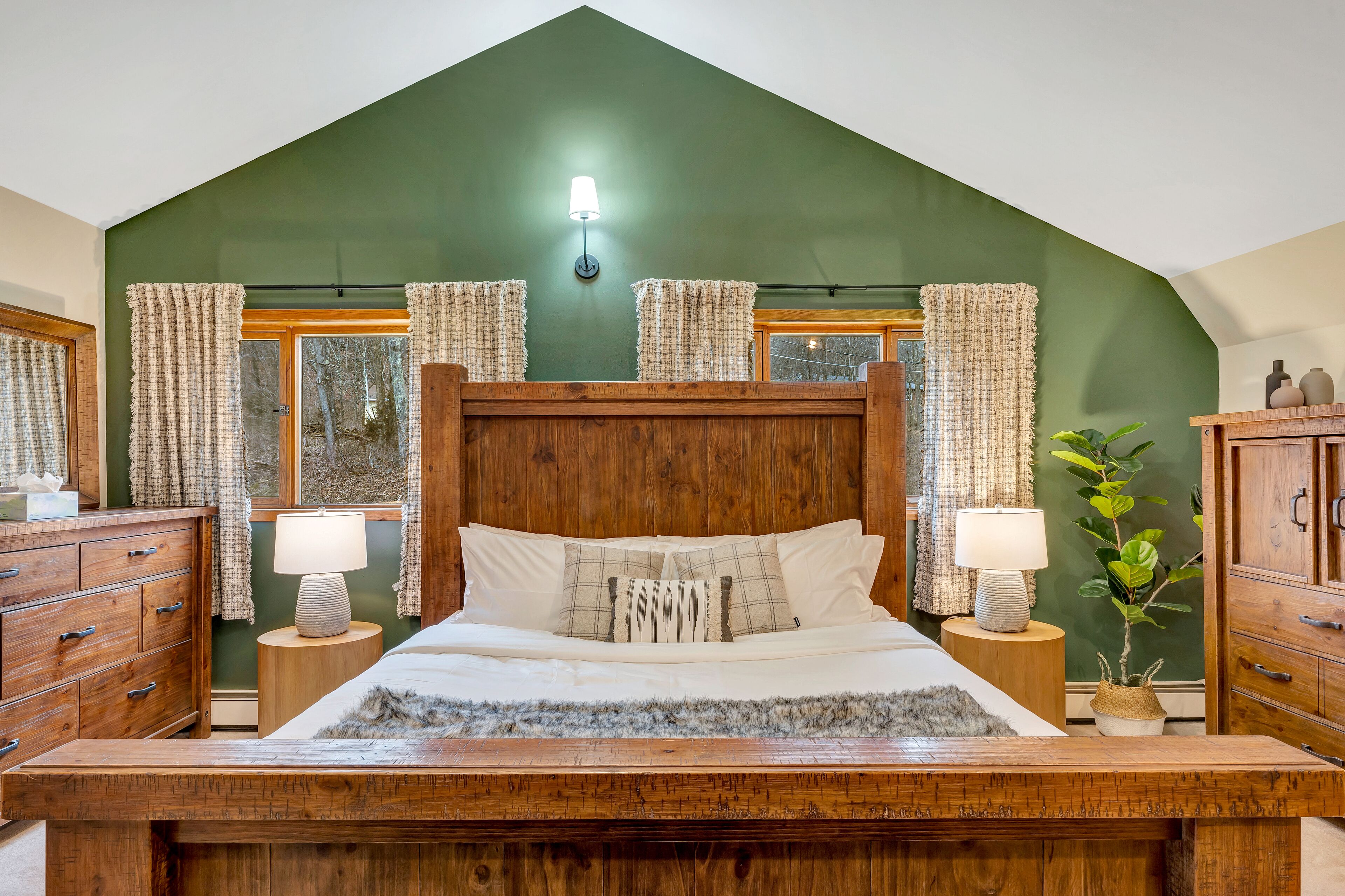 Een slaapkamer met een houten bed, twee nachtkastjes met lampen, een groene wand en een raam met gordijnen.