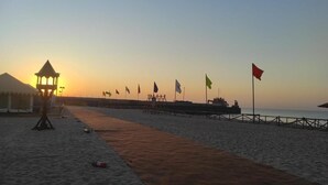 Una playa con un paseo marítimo de madera, un farol y banderas.