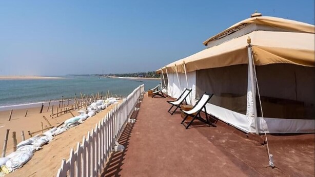 Un espacio con carpas a la orilla de la playa, con toldos blancos y sillones frente al océano.