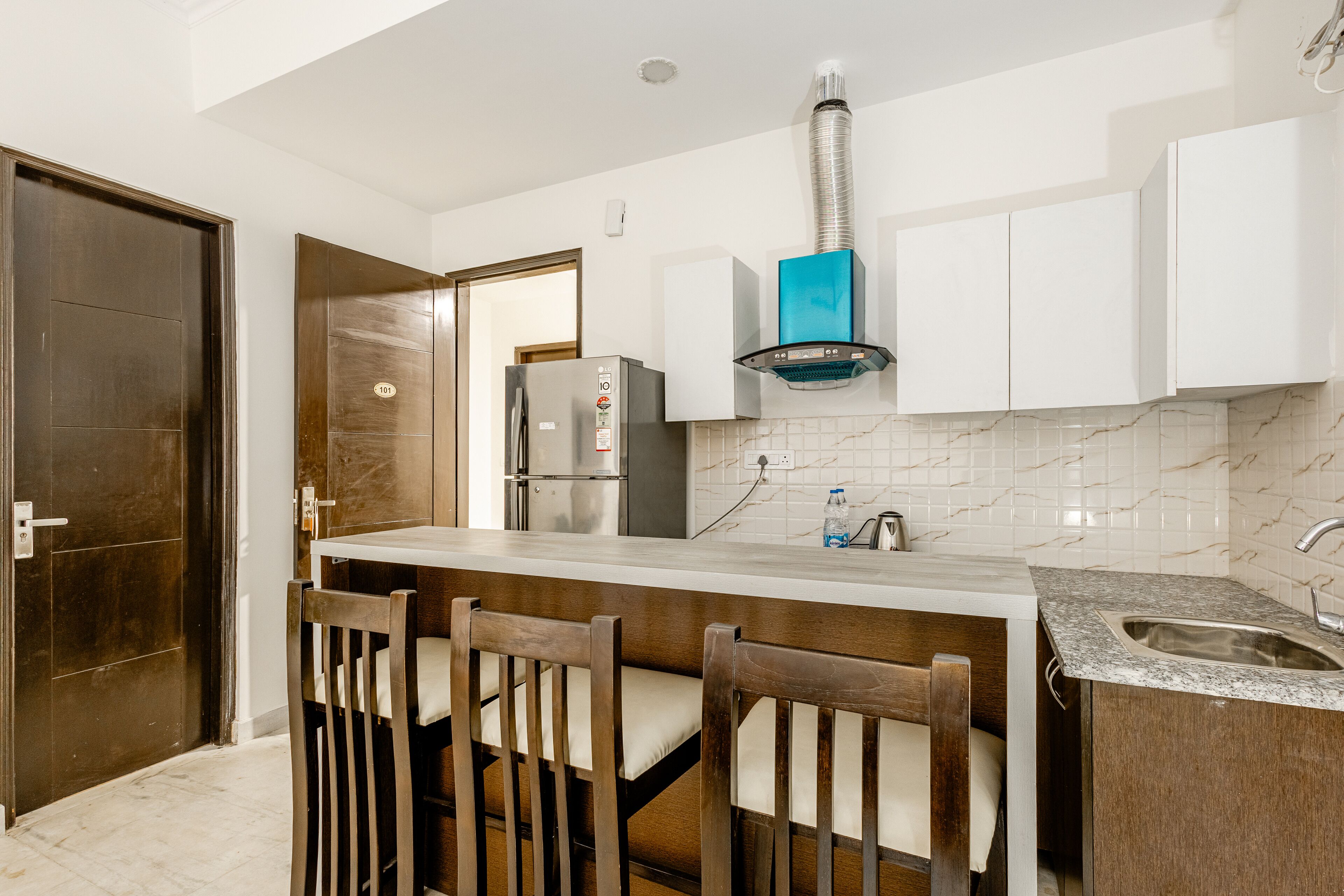 A modern kitchen with a built-in refrigerator, a blue ventilation hood, and a marble backsplash.