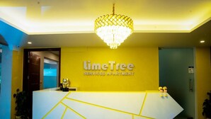 Un comptoir d’accueil agrémenté d’un lustre, une enseigne indiquant « LimeTree Serviced Apartment », et une porte située à gauche.