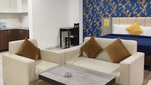 Une chambre d’hôtel moderne, dotée d’un canapé, d’une petite table basse, d’un lit avec une tête de lit bleue et d’un ventilateur de plafond.