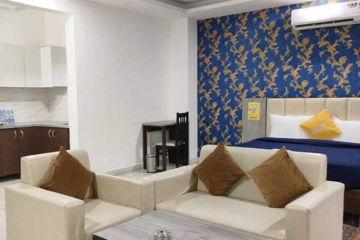 A modern hotel room with a sofa set, a small coffee table, a bed with a blue headboard, and a ceiling fan.