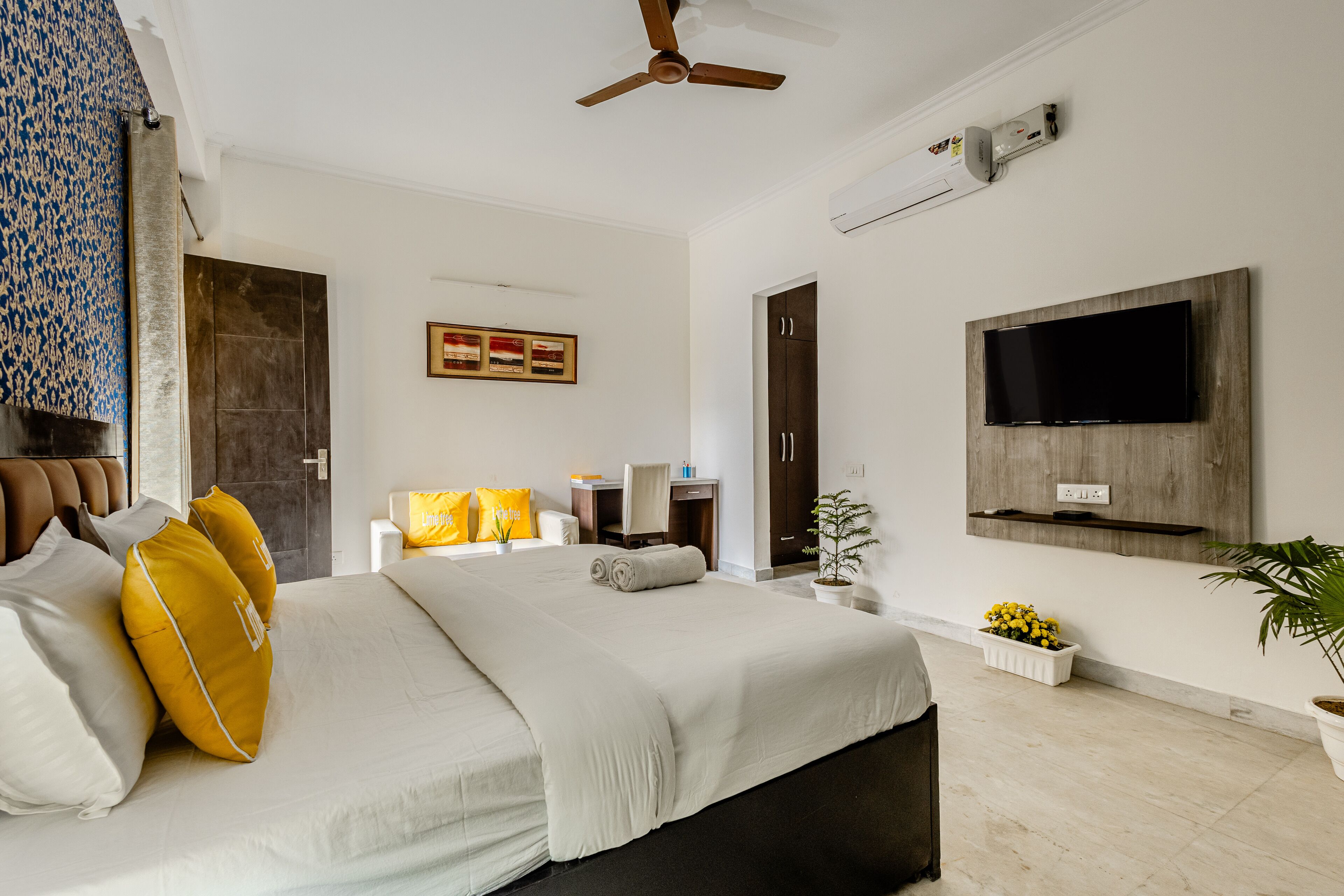 A modern hotel room with a large bed, a desk, a flat-screen TV, and a ceiling fan.