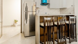 Une cuisine moderne avec un réfrigérateur en acier inoxydable, des chaises en bois, une hotte d’extraction bleue et des armoires blanches.