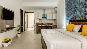 Une chambre d’hôtel moderne dotée d’un grand lit, d’un téléviseur fixé au mur, d’un coin cuisine avec des placards et d’un mur orné d’un motif.