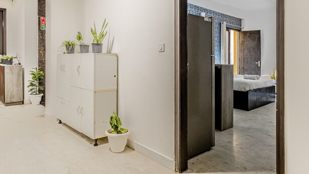 Un couloir avec une armoire blanche, des plantes en pot et un lit dans la pièce adjacente.