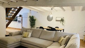 Ein modernes Wohnzimmer mit einer Eckcouch, einem Esstisch und einer Treppe, die in ein Obergeschoss führt.