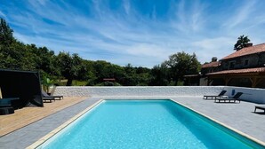 Ein rechteckiger Swimmingpool mit klarem, blauem Wasser, umgeben von einer weißen Mauer und einer Holzterrasse.