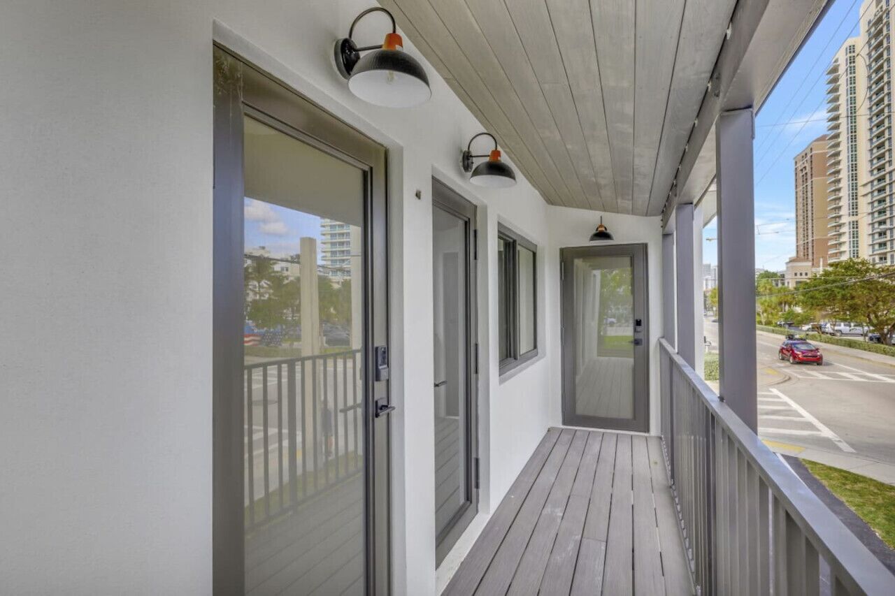 Un balcone coperto con porte e finestre in vetro, pavimento in legno e vista su una strada e degli edifici.