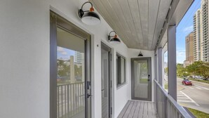 Ein überdachter Balkon mit Glastüren und -fenstern, Holzboden und Blick auf eine Straße und Gebäude.
