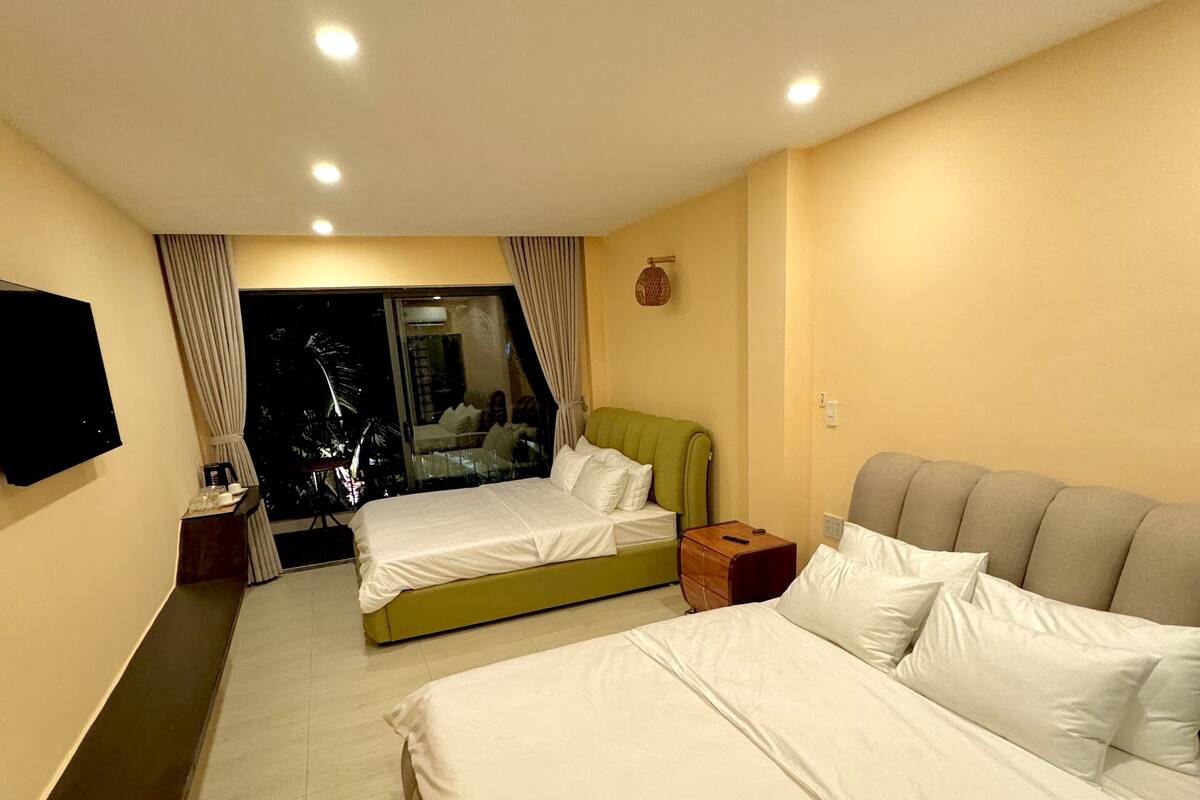 A hotel room with two beds, a TV, a window with curtains, and a ceiling light.