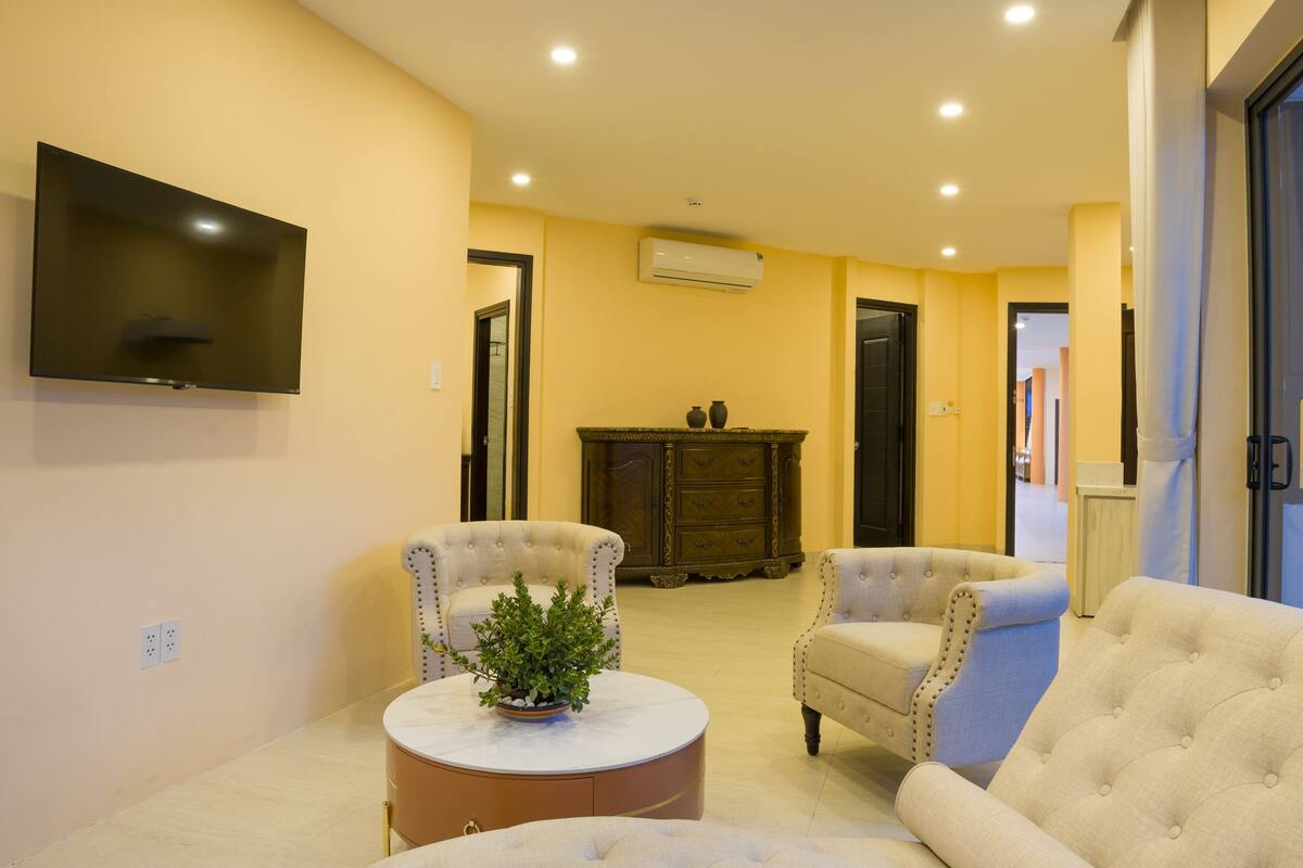 A living room with a flat-screen TV, two armchairs, a round coffee table with a plant, and a cabinet with decorative items.