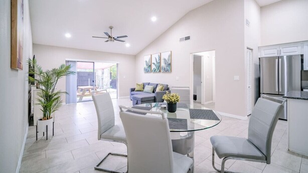 A spacious living area with a glass dining table, white sofas, and a modern kitchen with stainless steel appliances.