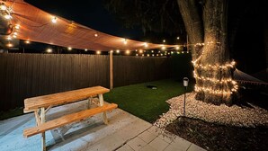 Ein Garten mit einem hölzernen Picknicktisch, Lichterketten, einer Hängematte und einem mit Lichtern umrankten Baum.