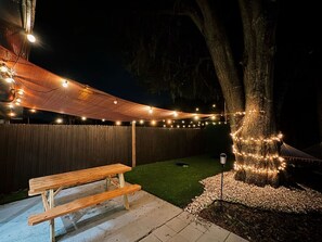 Ein Garten mit einem hölzernen Picknicktisch, Lichterketten, einer Hängematte und einem mit Lichtern umrankten Baum.