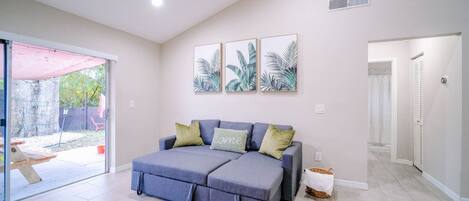 A room with a sofa, a sliding glass door leading to an outdoor area, and a wall with three framed pictures.
