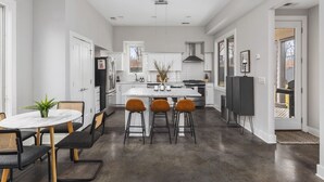 Una cocina moderna con armarios blancos, una isla central y una zona de comedor con una mesa redonda y taburetes de bar.