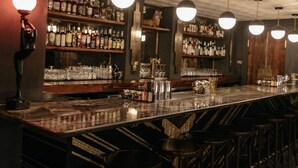 Un bar con una barra larga, estantes con botellas y lámparas colgantes.