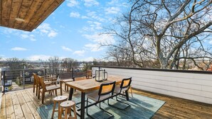 Terraza de madera con mesa y sillas, con vistas a un paisaje urbano con árboles.
