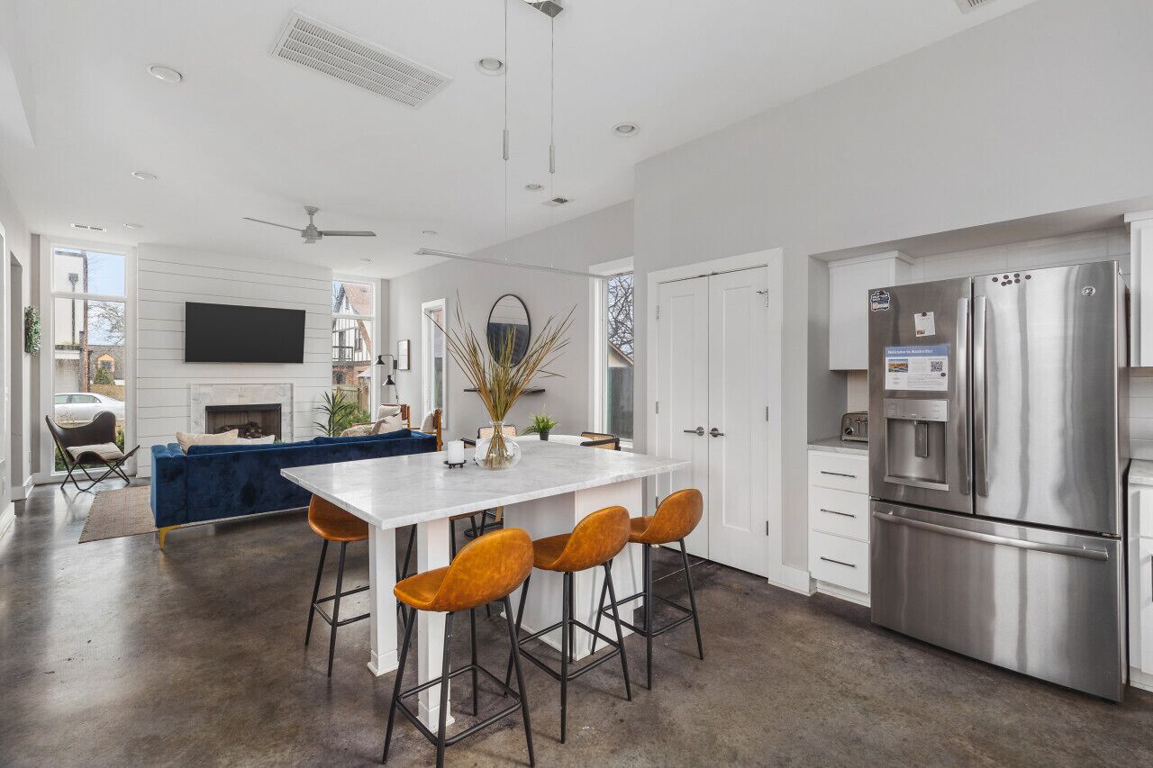 A modern kitchen with a large stainless steel refrigerator, a white island with bar stools, and a blue sofa in the background.