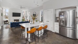 Una cocina moderna con un refrigerador de acero inoxidable grande, una isla blanca con taburetes de bar y un sofá azul al fondo.
