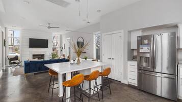 A modern kitchen with a large stainless steel refrigerator, a white island with bar stools, and a blue sofa in the background.